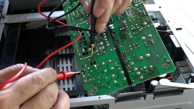 Electrician repairing a faulty sound equipment. Testing electric current on print circuit board, pcb with a multimeter.