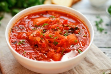 Appetizing Ukrainian and Russian borsch. Tomato soup in a white bowl. Vegan soup with tomato, sweet pepper, cabbage, carrots, beets and parsley. Food on a wooden background with textiles.