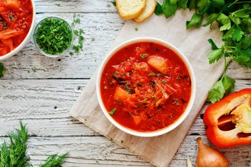 Appetizing Ukrainian and Russian borsch. Tomato soup in a white bowl. Vegan soup with tomato, sweet pepper, cabbage, carrots, beets and parsley. Food on a wooden background with textiles.