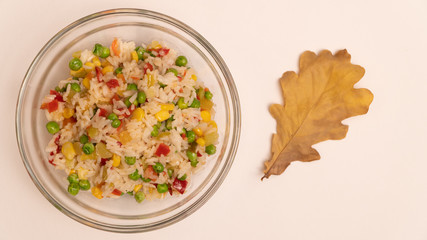 Cooked white rice vegetables in glass bowl with a dry oak leaf, top view with copy space.