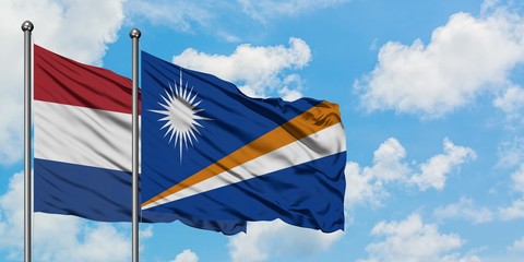Netherlands and Marshall Islands flag waving in the wind against white cloudy blue sky together. Diplomacy concept, international relations.