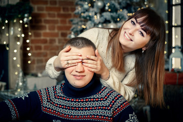 Beautiful girl closed eyes to a guy in a sweater on the background of the New Year tree