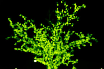 Green tree silhouette made of glowing blurry circles from New Year's bulbs on a black background.