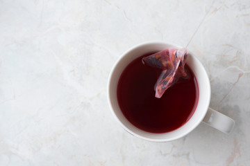 Making fruity tea in tea pyramid bag in white cup on marble background. Cozy winter breakfast mood, top view
