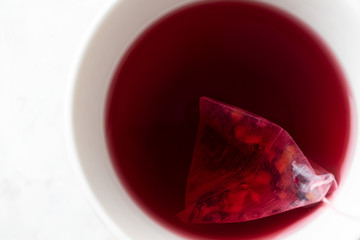Close-up tea pyramid bag with fruity tea in white mug on white background. Hot drink, top view