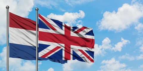 Netherlands and United Kingdom flag waving in the wind against white cloudy blue sky together....