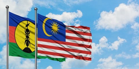 New Caledonia and Malaysia flag waving in the wind against white cloudy blue sky together. Diplomacy concept, international relations.