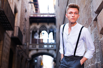 young European guy in shirt and trousers with suspenders walking around city