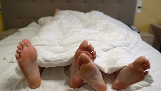 three pairs of legs in bed under a white blanket, playing