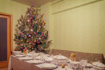 Served table with festive tableware near beautiful decorated Christmas tree in living room interior. Concept of new year holiday at cozy home. Selective focus, vintage tone