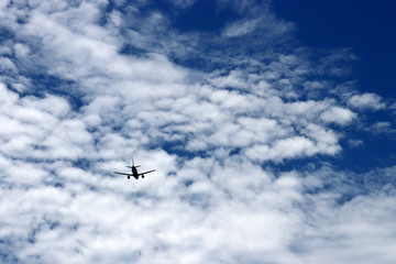 Airplane flying in the blue sky on background of white clouds, rear view. Silhouette of two-engine commercial plane during the turn, turbulence and travel concept