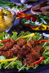 Barbecue with vegetables. The meat lies on the green leaves of the salad. In the background is bread, potatoes.