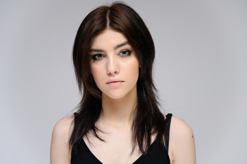Fototapeta premium Close-up portrait of a young pretty girl with long black hair, clean skin on a gray background. The concept of cosmetics for the face, great makeup, fashionable hairstyle.