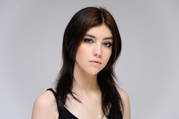 Fototapeta premium Close-up portrait of a young pretty girl with long black hair, clean skin on a gray background. The concept of cosmetics for the face, great makeup, fashionable hairstyle.