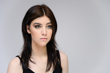 Fototapeta premium Close-up portrait of a young pretty girl with long black hair, clean skin on a gray background. The concept of cosmetics for the face, great makeup, fashionable hairstyle.