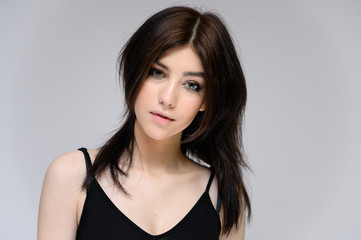 Naklejka premium Close-up portrait of a young pretty girl with long black hair, clean skin on a gray background. The concept of cosmetics for the face, great makeup, fashionable hairstyle.