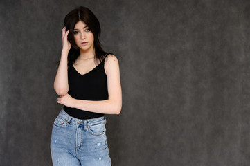 Portrait of a young pretty girl student with long black hair, on a gray background. He stands right in front of the camera, showing his hands in different poses with different emotions.