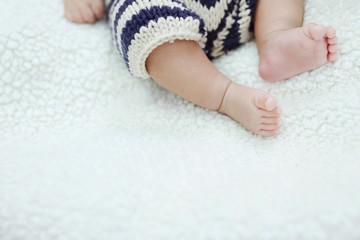 Close up Newborn baby feet small tiny adorable bare pink with Wearing pants, knitting dresses. Little infant with cute on bed sheet Soft wool on white blanket, above view. Space for text. soft focus.