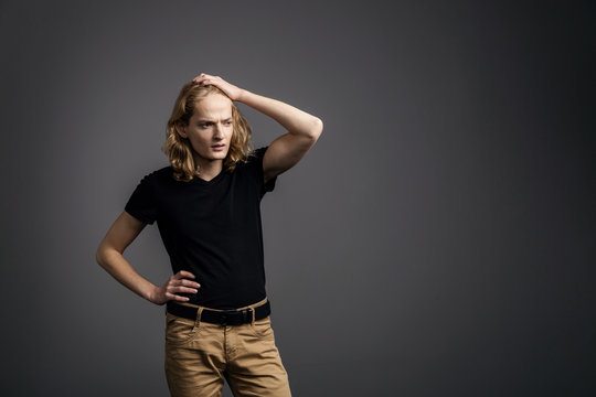 A young guy with long blonde hair looking very puzzled. A young man is showing something on a gray background.