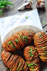 Fototapeta na wymiar Hasselback potatoes.Horizontal view, Appetizing potato accordion baked in the oven. Potato on a wooden background.