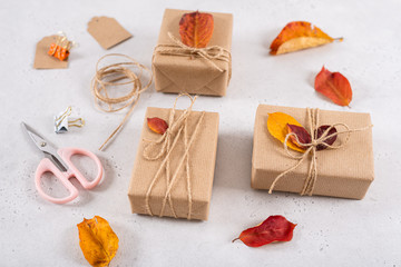 Autumn vibes, thanksgiving day presents, seasonal sale concept. Fall composition with presents in craft paper decorated with dried leaves on white background. Side view