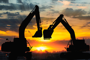 Silhouettes two excavator with sunlight background of sunset in cityscape © chaphot