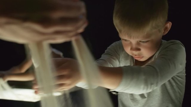 Medium shot of focused little boy and unrecognizable female art teacher pouring sand on light table while making animation in class