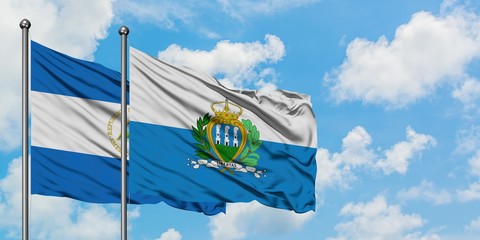Nicaragua and San Marino flag waving in the wind against white cloudy blue sky together. Diplomacy concept, international relations.