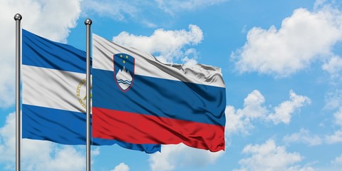Nicaragua and Slovenia flag waving in the wind against white cloudy blue sky together. Diplomacy...