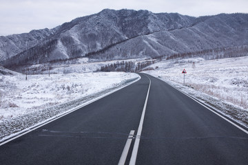 A picturesque mountain road stretching into the distance to the mountains covered with dense fog.