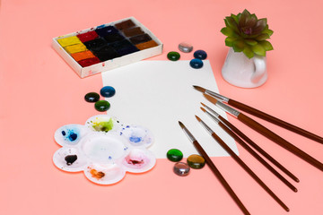 Brushes, watercolors, houseplant and a blank sheet of paper for painting. Layout on the theme of art