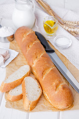 Freshly baked homemade french baguette with a brown crust on paper on a white wooden background.