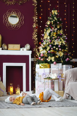 Cozy little sister children in white warm sweaters and knitted hats in the Christmas interior, con