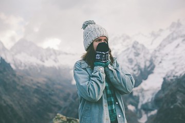 Fototapeta na wymiar Young traveler girl in gloves standing over mountain peaks and warming cold hands