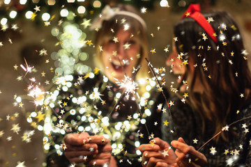   Portrait of 2 young women with glamor clothes and confetti and sparklers celebrating a party together with sparklers and lights