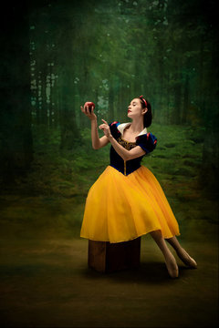 Young ballet dancer as a Snow White with poisoned apple in forest. Flexible caucasian ballerina dances like character of fairytail in bright clothes. Adorable and elegance story in motion and dancing.