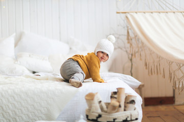 Toddler kid in a hat and sweater gets off the bed