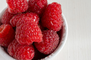 Top view of red raspberries with water drops, in white bowl in horizontal