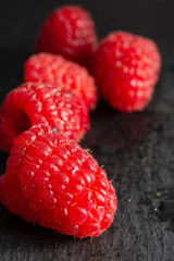 Close-up of red raspberries, the first one focused on the other out of focus, on a blackboard background, vertically