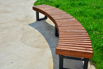 Curved wooden bench in the park. Empty bench in the summer park.