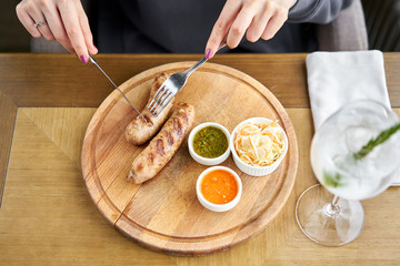 Lunch in a restaurant, a woman cuts Grilled sausages. Serving on a wooden Board. Barbecue restaurant menu, a series of photos of different meats. Pickled cabbage and two sauces