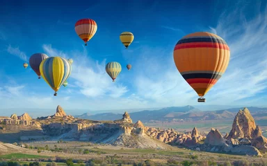 Deurstickers Ballon Kleurrijke heteluchtballonnen vliegen in de blauwe lucht over verbazingwekkende valleien met sprookjesachtige schoorstenen in Cappadocië, Turkije