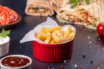 Red bowl of french fries chips potato and sauces on black background.