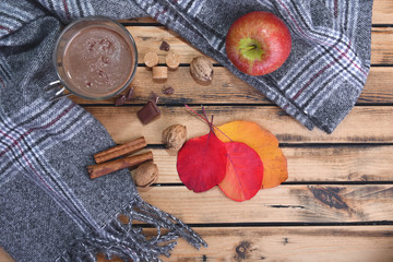 mug of hot chocolate with scarf and red apple in winter and on a wooden table