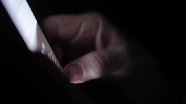 Pale skined hand scrolls through phone in the dark