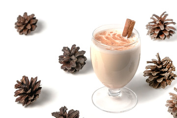 Eggnog Christmas cocktail in a transparent glass, sprinkled with grated nutmeg, on white background, isolated, decorated with spruce cones.