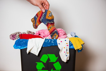 Hand putting used sock in bin with recycling sign. Person in the house separating waste. Heap of...