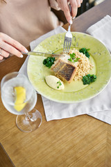 Roasted Pike perch with spelt and Polish sauce. Lunch in a restaurant, a woman eats delicious and healthy food. Dish decorated with a spinach. Restaurant menu
