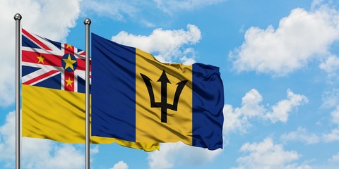 Niue and Barbados flag waving in the wind against white cloudy blue sky together. Diplomacy concept, international relations.