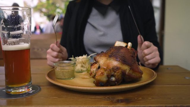 Woman enjoying traditional Czech food Roasted pork knee knuckle - Pecene veprove koleno - With light beer in a restaurant closeup